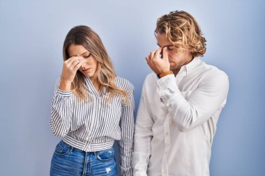Young couple standing over blue background tired rubbing nose and eyes feeling fatigue and headache. stress and frustration concept. 