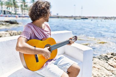Genç İspanyol adam klasik gitar çalıyor sahildeki bankta oturuyor..