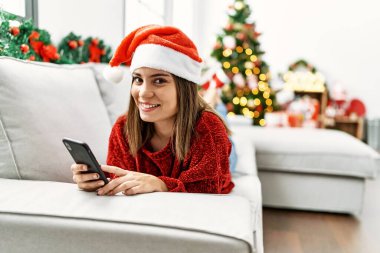 Evdeki Noel ağacının yanındaki koltukta akıllı telefon kullanan İspanyol genç kız..