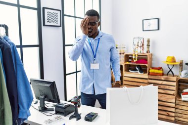 Young african man working as manager at retail boutique yawning tired covering half face, eye and mouth with hand. face hurts in pain. 