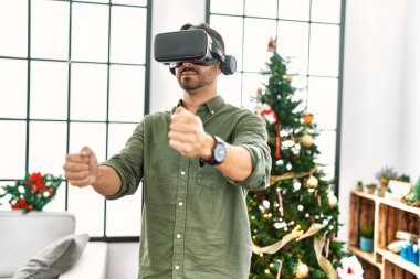 VR gözlük takan genç İspanyol adam Noel ağacının yanında duruyor.