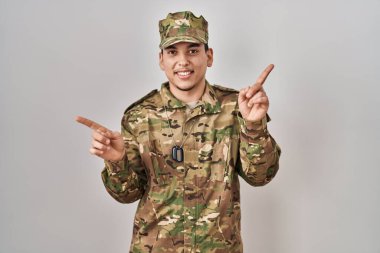 Young arab man wearing camouflage army uniform smiling confident pointing with fingers to different directions. copy space for advertisement 