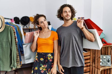 Satış mağazasında alışveriş torbaları tutan genç İspanyol çift gülümseyip yan tarafa bakıyor ve düşünüyor.. 