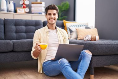 Genç İspanyol adam dizüstü bilgisayar kullanıyor ve evde kahve içiyor.