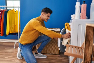 Young hispanic man washing clothes at laundry