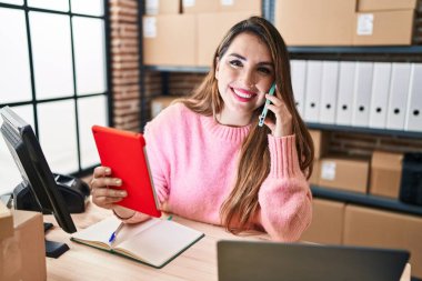 Genç ve güzel bir İspanyol kadın. İş kadını. Ofiste akıllı telefondan konuşan bir dokunmatik ped kullanıyor.