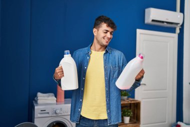 Çamaşır odasında çamaşır deterjanı şişeleriyle çamaşır yıkayan İspanyol genç adam.