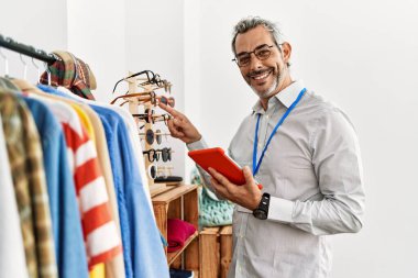 Orta yaşlı, gri saçlı bir dükkan asistanı giyim mağazasında dokunmatik ped kullanıyor.