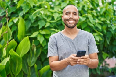 Parkta akıllı telefon kullanarak gülümseyen genç Latin adam.
