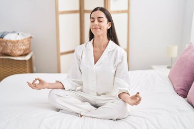 Genç İspanyol kadın yoga egzersizi yapıyor. Yatak odasında oturuyor.