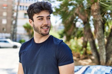 Genç İspanyol adam gülümseyerek şehirde mutlu mesut dikiliyor..