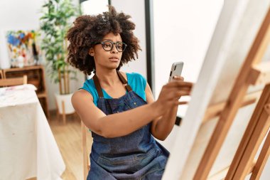 Genç Afrikalı Amerikalı kadın, resim stüdyosunda akıllı telefon çizimiyle resim yapıyor.