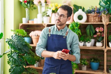 Çiçekçide akıllı telefon kullanarak gülümseyen İspanyol çiçekçi.