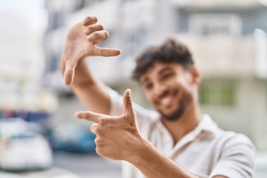 Young arab man smiling confident doing photo gesture with hands at street