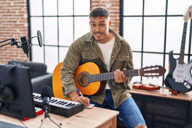 Young hispanic man musician composing song playing classical guitar at music studio