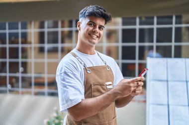 Genç İspanyol garson, kahvecinin terasında akıllı telefon kullanarak gülümsüyor.