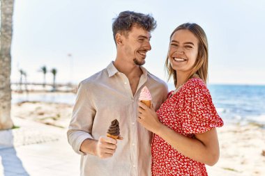 Genç İspanyol çift tatilde gülümseyerek kumsalda dondurma yiyor.