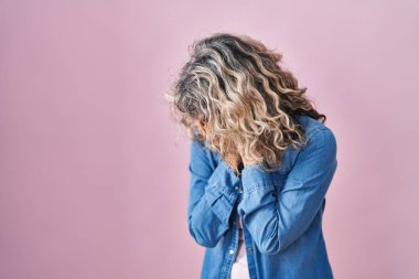 Orta yaşlı bir kadın pembe arka planda duruyor. Ağlarken suratını ellerle kapatıyor. depresyon kavramı. 