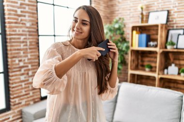 Young hispanic woman smiling confident combing hair at home