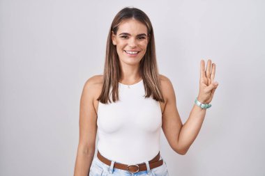 Hispanic young woman standing over white background showing and pointing up with fingers number three while smiling confident and happy. 