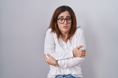 Esmer kadın, izole edilmiş beyaz arka planda duruyor. Kış soğuğu yüzünden titriyor ve donuyor. Yüzünde üzgün ve şok ifadesi var. 