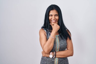 Beyaz arka planda duran olgun İspanyol kadın kameraya kollarını kavuşturup gülümseyerek ve çenesini kaldırarak bakıyor. Olumlu düşünmek. 