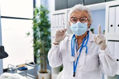 Gri saçlı, doktor üniforması giyen ve elinde şırınga tutan yaşlı bir kadın bir fikir ya da soru işareti ile şaşırdı. 