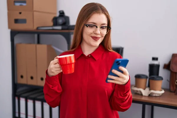 Młoda Ruda Kobieta Biznes Pracownik Pomocą Smartfona Picia Kawy Biurze — Zdjęcie stockowe