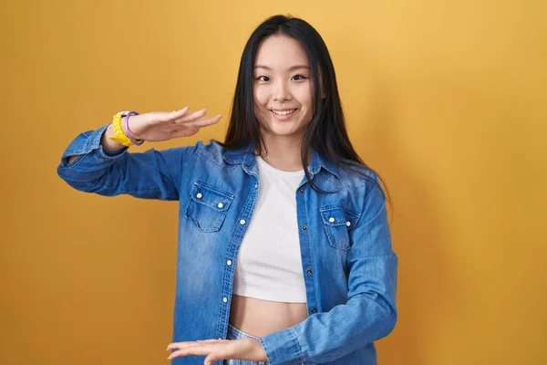 Young Asian Woman Standing Yellow Background Gesturing Hands Showing Big — Zdjęcie stockowe