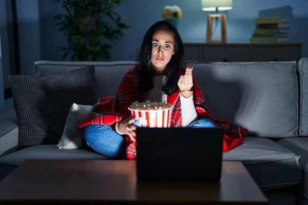 Hispanic woman eating popcorn watching a movie on the sofa doing italian gesture with hand and fingers confident expression