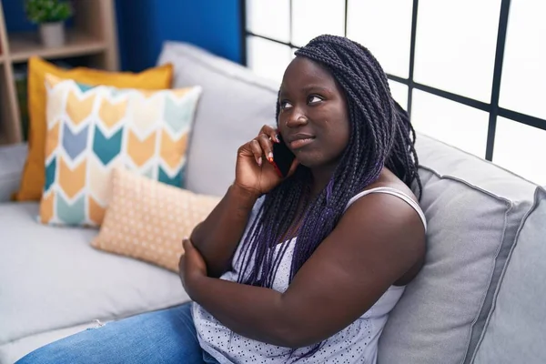 African american woman talking on smartphone with worried expression at home