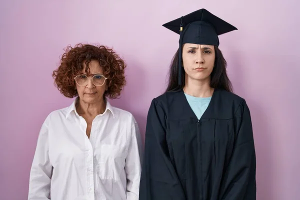 ヒスパニック系の母親と娘の卒業キャップと式のローブを着て懐疑的で緊張し 問題のために動揺を眉をひそめて 否定的な人 — ストック写真