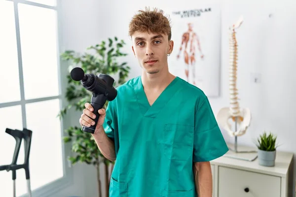 Young Caucasian Physio Man Holding Muscle Percusion Gun Clinic Thinking — Stok fotoğraf