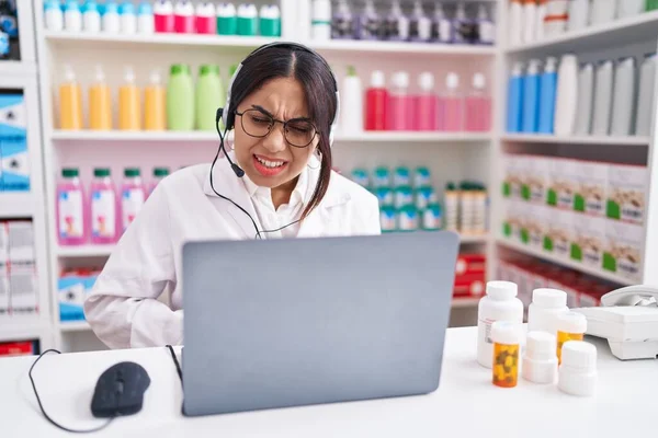 Young arab woman working at pharmacy drugstore using laptop with hand on stomach because indigestion, painful illness feeling unwell. ache concept.