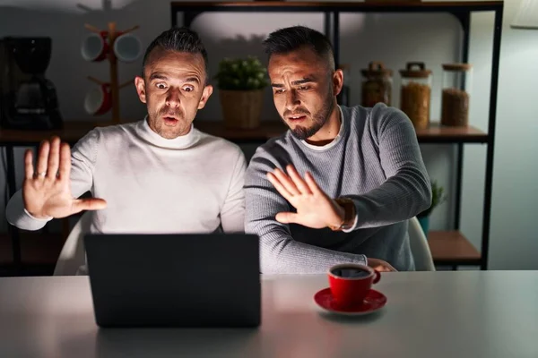 Homosexual couple using computer laptop doing stop gesture with hands palms, angry and frustration expression