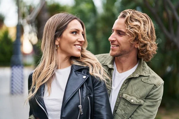 Kadın ve erkek gülümsüyor. Parkta birbirlerine sarılıyorlar.