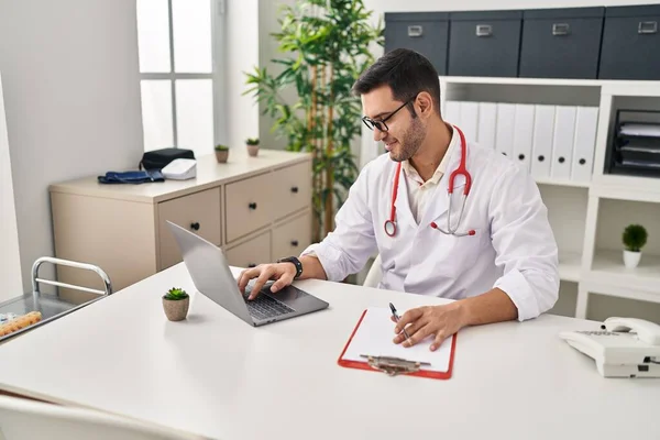 Joven Hispano Vistiendo Uniforme Médico Usando Laptop Trabajando Clínica —  Fotos de Stock