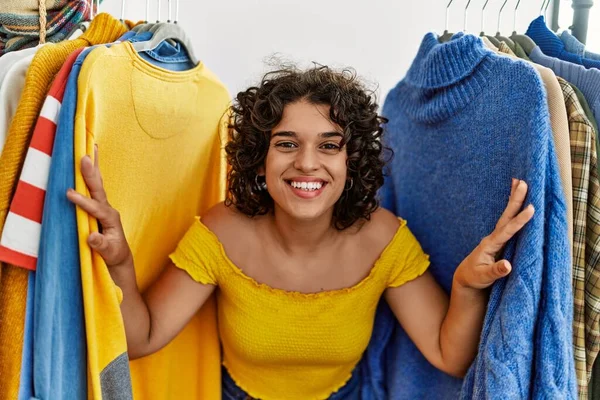 Young latin customer woman smiling happy appearing through clothes at clothing store.