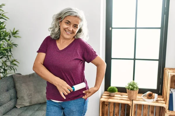 Middle age grey-haired woman using pet hair remover roller at home.
