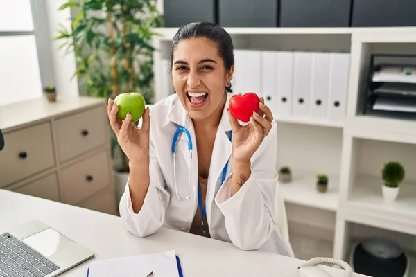 Young Hispanic Woman Working Dietitian Clinic Holding Green Apple Smiling —  Fotos de Stock