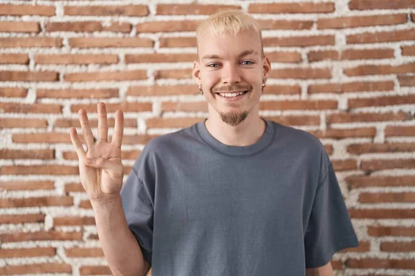 自信と幸せな笑顔ながら 若い白人男性はレンガの壁に立って指の数4を示すと指摘します — ストック写真
