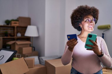 Yeni evde akıllı telefon ve kredi kartı kullanan Afrikalı Amerikalı bir kadın.