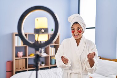 Koyu renk saçlı İspanyol kadın akıllı telefonuyla güzellik dersi kaydediyor. Gururla bağırıyor, zaferi kutluyor ve kollarını kaldırarak başarıyı kutluyor. 