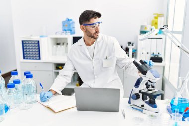 Mikroskop ve laptopla laboratuvarda bilimsel olarak çalışan yakışıklı bir İspanyol.