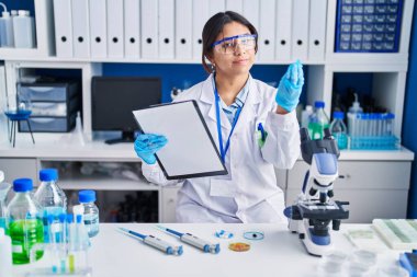Hispanic young woman working at scientist laboratory doing italian gesture with hand and fingers confident expression 