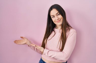 Pembe arka planda duran genç esmer kadın gülümseyerek doğal bir şekilde içeri girmeye davet ediyor. 