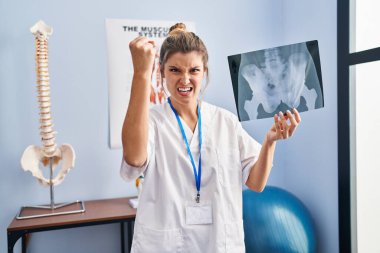 Leğen kemiği radyografisi tutan genç bir kadın öfkeyle bağırıyor, öfkeyle bağırıyor ve el kaldırıyor. 