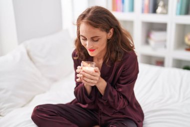 Genç, güzel, İspanyol bir kadın yatakta oturuyor. Yatak odasında aromatik mum kokuyor.