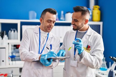 Two men scientists writing on document holding test tube at laboratory