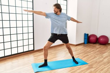 Orta yaşlı beyaz bir adam spor merkezinde yoga eğitimi alırken gülümsüyor.